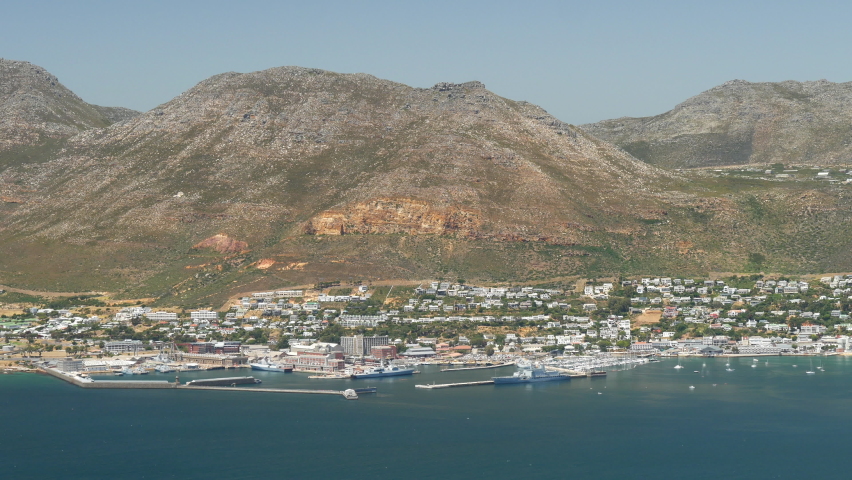 High angle long shot Simonstown harbor, naval base, blue ocean, sailboats, mountainside homes, mountain skyline