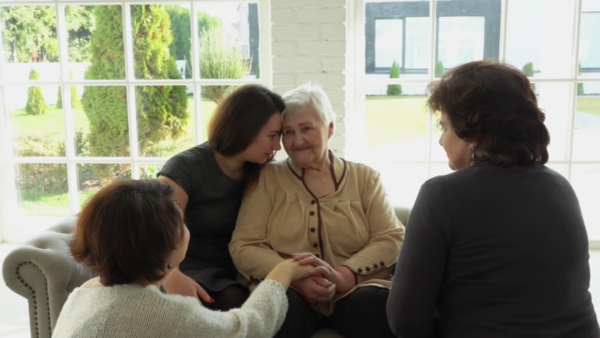 The multi-generations family enjoys togetherness. An elderly white-haired woman is sitting with her daughter and granddaughters in hall with wide windows.  | Shutterstock HD Video #1066134175