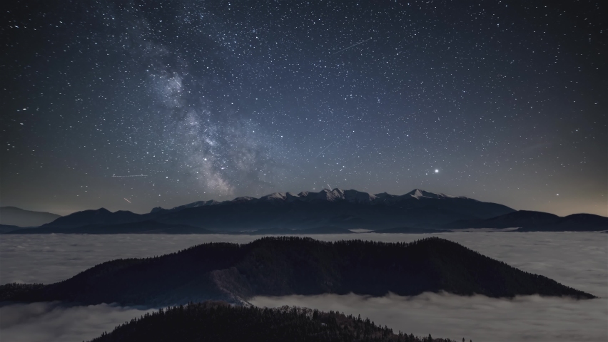 Milky way galaxy in starry night sky over snowy winter alps mountains above foggy clouds landscape Astronomy Time lapse