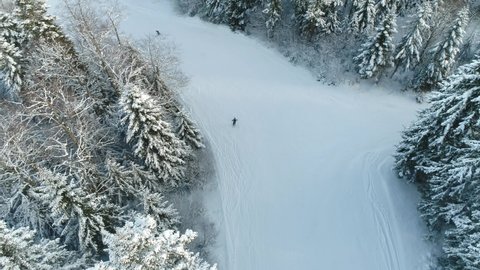 Aerial footage of a mountain in winter with skiers on the tracks, the shot is tracking the skiers down the slope