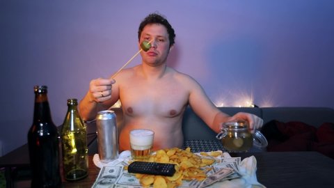 A drunkard watches TV, drinks beer and eats pickles cucumber