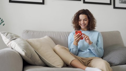 Happy hispanic teen girl holding cell phone using smartphone device at home. Smiling young latin woman blogger subscribing new social media, buying in internet, ordering products online in apps.
