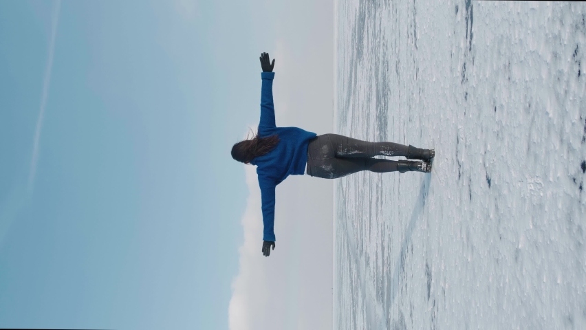 Vertical video of millennial woman professional dancer, dancing energetic jazz funk or hip hop on frozen lake in cold winter. Female hipster dances challenge for social networks on snow-covered river