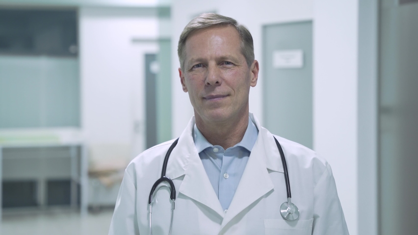 Happy trustworthy proud mature old medical professional doctor stands arm crossed in hospital. Middle aged male senior physician practitioner wears white coat, stethoscope looking at camera. Portrait Royalty-Free Stock Footage #1066143274