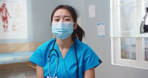Attractive young nurse in medical protective mask making video blog in hospital. Asian female blogger wearing blue uniform speaking on camera, giving advice to viewers. Pandemic, social media.