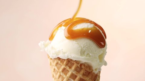 melted caramel sauce flowing on vanilla ice cream scoop in waffle cone close up on beige background. perfect summer dessert