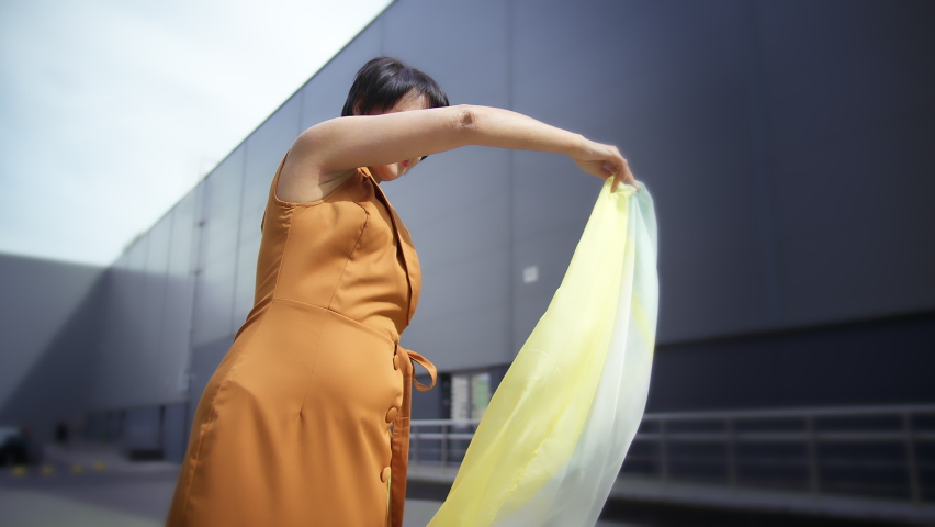 pretty woman playing with a scarf on the street and looking at the camera, stylish woman outdoors