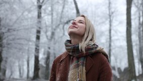 Blonde woman in scarf and coat stay in a park in snowfall
