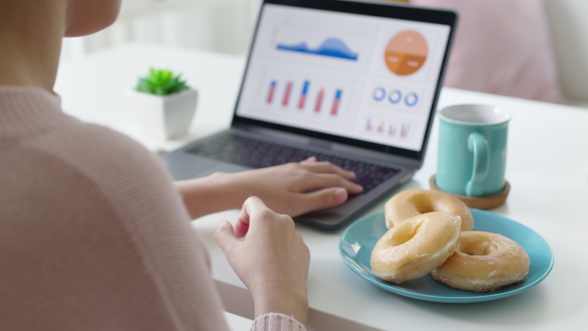 Young attractive beautiful asian female hungry eat doughnut take away snack food with full mouth look at computer notebook at home in busy work from home multitask unhealthy meal lifestyle concept. | Shutterstock HD Video #1066146721