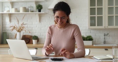 Happy 30s young caucasian woman in eyeglasses calculating paper domestic utility bills, making payment online on computer e-banking applications, feeling satisfied with good financial service at home.