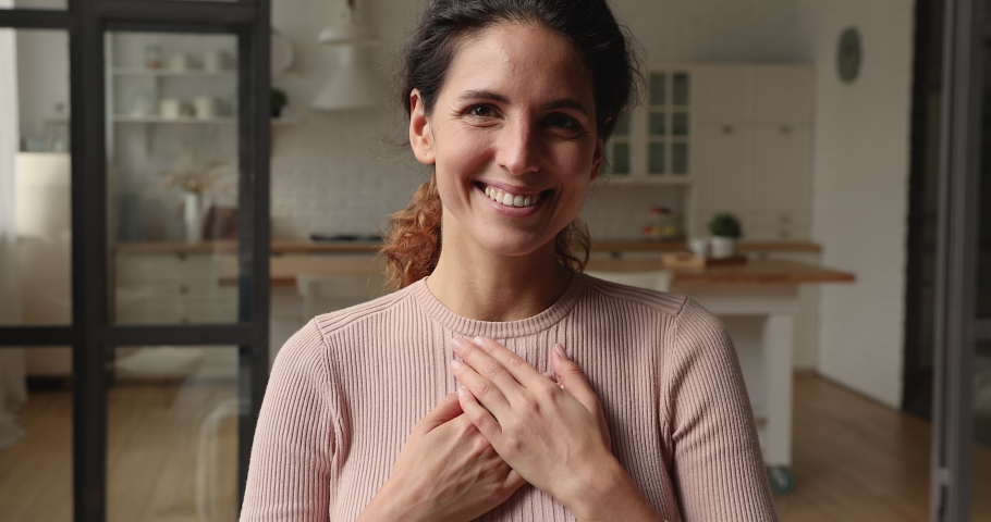 Smiling sincere kind young caucasian woman holding folded hands on heart chest, feeling deeply thankful at home. Happy inspired beautiful millennial lady showing gratitude, expressing appreciation. Royalty-Free Stock Footage #1066149646