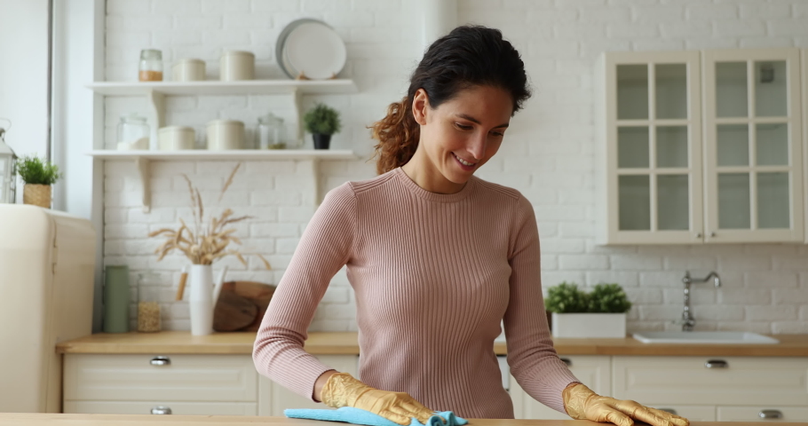Smiling millennial beautiful housewife wearing rubber gloves, involved in wiping kitchen surfaces at home, keeping house neat. Happy professional female cleaning worker mopping dust indoors. | Shutterstock HD Video #1066149919