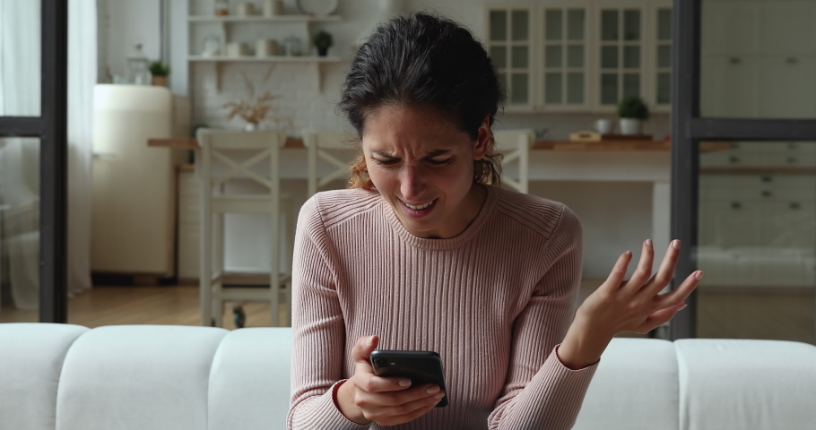 Confused young woman looking at mobile phone screen, feeling stressed of getting message with unpleasant scam news. Unhappy millennial caucasian lady dissatisfied with bad smartphone device work. | Shutterstock HD Video #1066150201