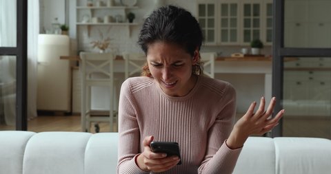 Confused young woman looking at mobile phone screen, feeling stressed of getting message with unpleasant scam news. Unhappy millennial caucasian lady dissatisfied with bad smartphone device work.