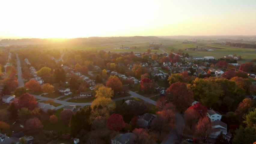Establishing shot of small town homes set among rural farm fields at sunrise. 1970s housing development featured in autumn fall foliage.