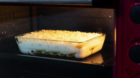 Gratin with pasta Bechamel and grated cheese in glass casserole baking in the oven time-lapse Shot