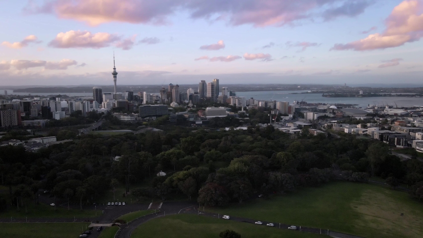 Auckland Domain park, sky tower and cityscape under wispy colorful clouds, dolly in 