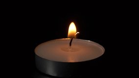 Macro burning small round candle flame isolated on black background, 4K video