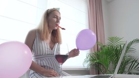 Young beautiful blonde girl congratulates on her birthday online and blows a festive whistle. Communication on social networks. Communication during a pandemic.