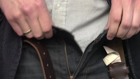 
A man fastens his trousers and leather belt after peeing, tucks his shirt in pans, fixes his underwear, pulls up a zip,  buttons up, and straightens a deep blue corduroy jacket over black jeans