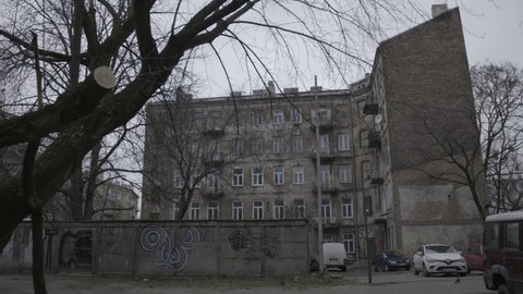 A Jewish Ghetto building behind bare, winter trees with graffiti on the walls and some cars parking in the courtyard, a 4K (Sony S-Log) video clip, February 25th, 2020, Warsaw, Poland.