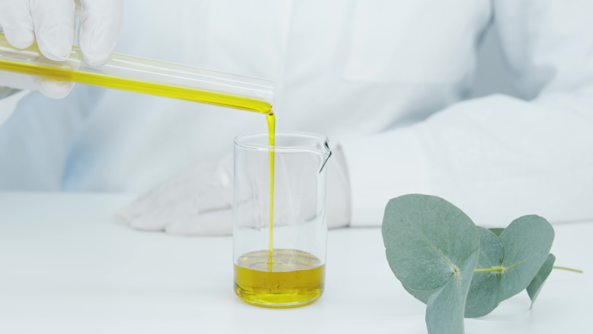 The beautician pours natural oil from a test tube into a glass from a test tube. Eucalyptus branch on the table. Production of essential oils, natural cosmetics and creams. | Shutterstock HD Video #1066162495