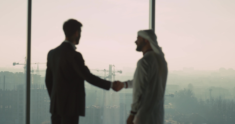 Collaboration people. Young successful businessman making agreement corporate business deal with Arabian entrepreneur standing by window. | Shutterstock HD Video #1066163848