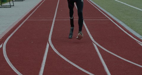 Crop view of disabled male person with prosthetic running blade at track on sports field. Amputee male sportsman jogging. Concept of motivational sports footage, paralympic