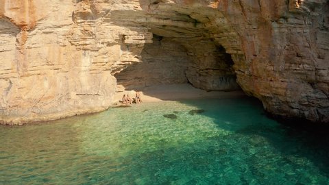 A couple of travelers swims in a hidden cove with a cave in mountain on the road from Demre to Antalya, Turkey. Aerial view 4K.