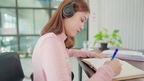 A young Asian university student wearing headphones to study online at home,During the time of the virus outbreak and did not attend university.