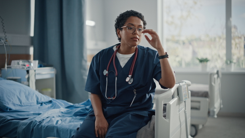 Hospital Ward: Portrait of Sad, Tired Black Nurse Sitting on a Bed, Holding Her Head in Sorrow for all the Patients that Couldn't Be Saved in Pandemic. During Tragic Times Brave Paramedics Save Lives Royalty-Free Stock Footage #1066174312