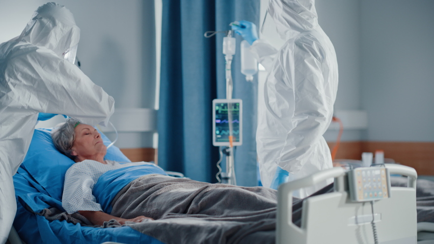 Hospital Coronavirus Emergency Department Ward: Team of Doctors wearing Coveralls, Face Masks Take Care of a Senior Patient Lying in Bed, Put Oxygen Mask and Connect Iv Drip. Medics Saving Lives Royalty-Free Stock Footage #1066174405