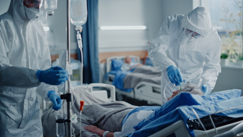 Hospital Coronavirus Emergency Department Ward: Team of Doctors wearing Coveralls, Face Shields Take Care of a Senior Patient Lying in Bed, Put Oxygen Mask and Lung Ventilator. Medics Saving Lives Royalty-Free Stock Footage #1066174459