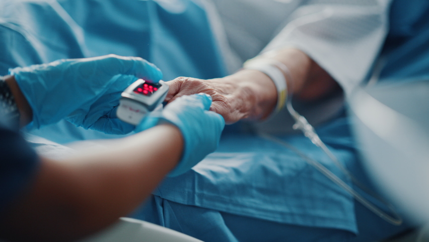 Hospital Ward: Senior Female Resting in a bed Nurse Puts on Finger Heart Rate Monitor, Pulse Oximeter showing Pulse. Anonymous Nurse Checks Vitals of Woman Getting well after Surgery. Focus on Hands Royalty-Free Stock Footage #1066174510