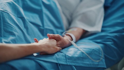 Hospital Ward: Senior Woman Resting and Recovering in Bed, Caring Daughter Holds Her Fragile Hand in Gesture of Support and Comforting. Focus on the Hands. Deeply Emotional Cinematic Shot