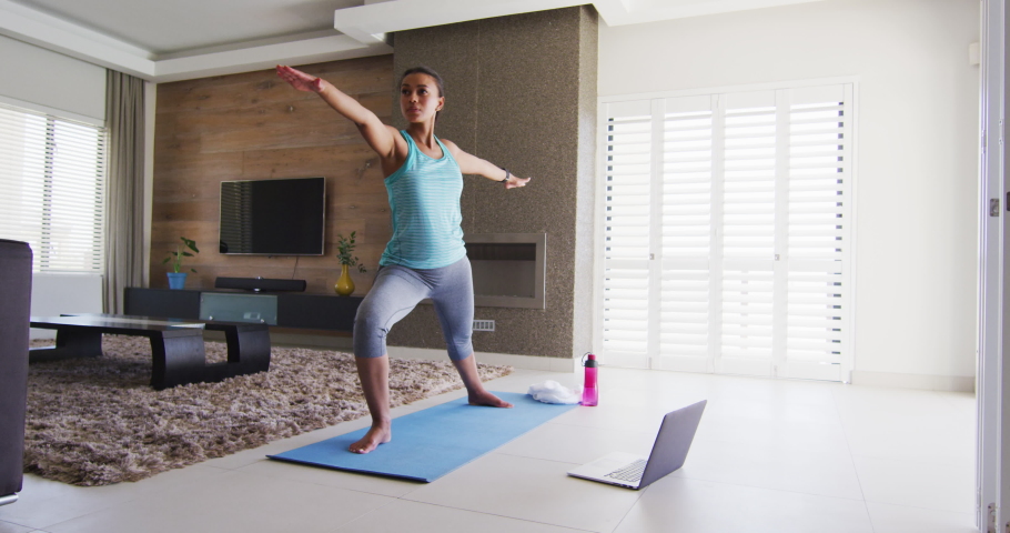 Mixed race woman excercising on a mat with laptop. enjoying quality time at home self isolating in quarantine lockdown.