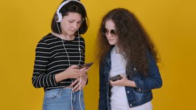 Young girls teenagers use smartphones listen to music isolated on yellow background.