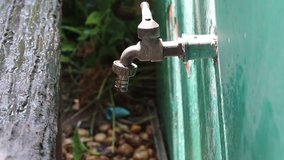 Hands using screwdriver tighten clip with rubber hose to the metal faucet on cement closeup.