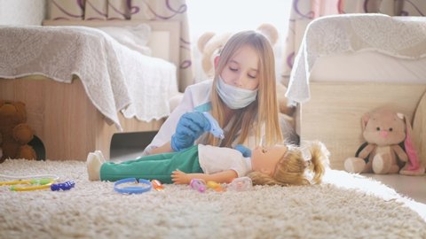 Beautiful little girl playing doctors with doll at home.