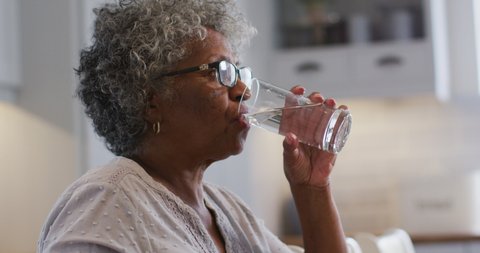 Senior african american woman taking medication and drinking water while sitting at home. staying at home in self isolation in quarantine lockdown