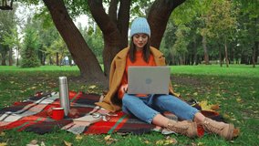 smiling freelancer having video call on laptop during picnic in park