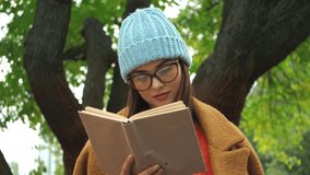 young woman reading book and smiling while looking at camera in park