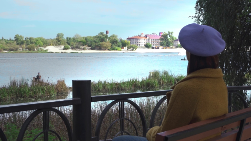 young woman sitting on bridge in park and looking at river