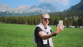 Woman making video call from beautiful nature park in front of mountains. She sharing impressions from her trip.
