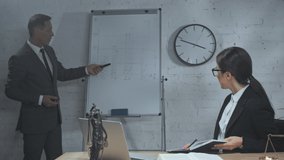Lawyer pointing at flipchart near colleague with notebook in office