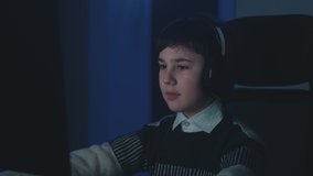 Scared boy in headphones shocked by terrible scene while watching horror video on computer. Afraid schoolboy kid look at monitor screen, cover mouth with his hand while using laptop late at night