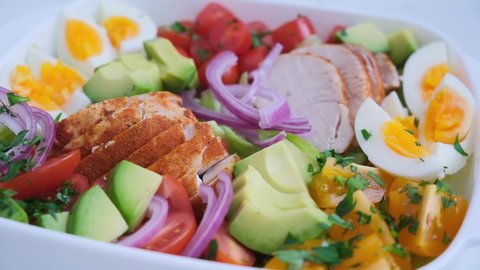 American cobb salad with chicken, avocado, egg, tomatoes and onions in white dish, light background. American cuisine concept.