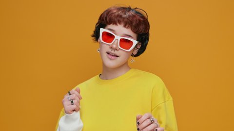 Dancing Girl Teenager Asian on a Yellow Background in yellow clothes with Glasses with Piercings Smiling Rhythmically moving in Dance Sings slow motion. Portrait. Joy. Lifestyle. Positive emotion