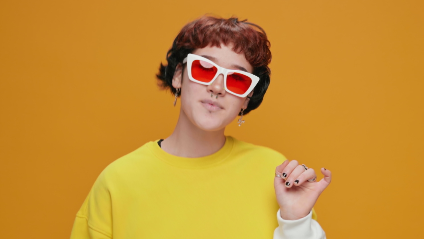 Dancing Girl Teenager Asian on a Yellow Background in Yellow clothes with Glasses with Piercings Smiling Rhythmically Moving in Dance Sings slow motion. Portrait. Joy. Lifestyle. Positive Emotion