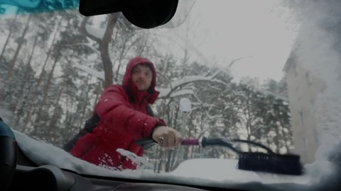 A man cleans the car from snow, a view from the inside of the car. Sweep the snow off the windshield. View from the cockpit. The car is covered with snow after a blizzard.
